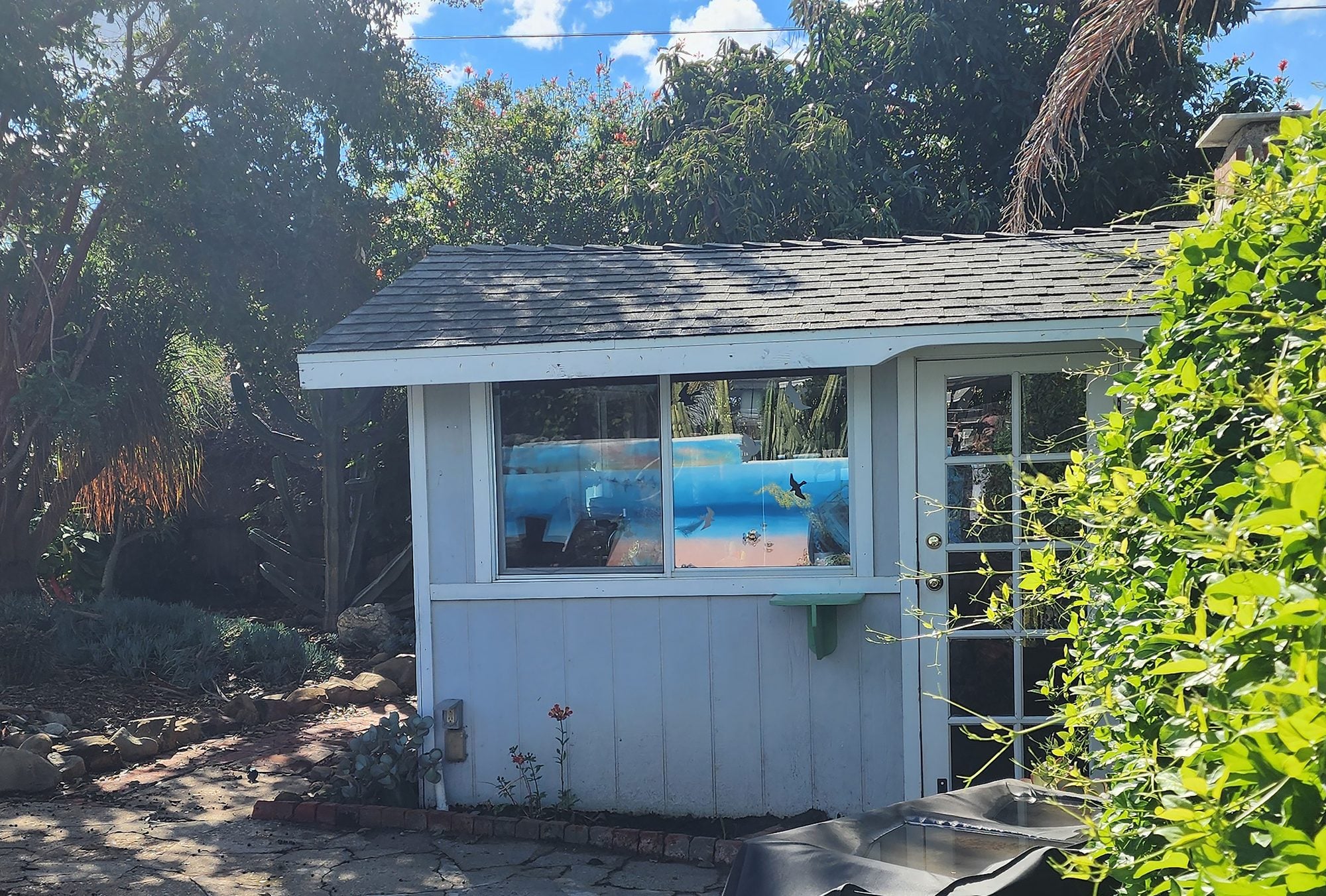 The SlowLine Art Room studio, a small white garden studio with French doors, surrounded by trees