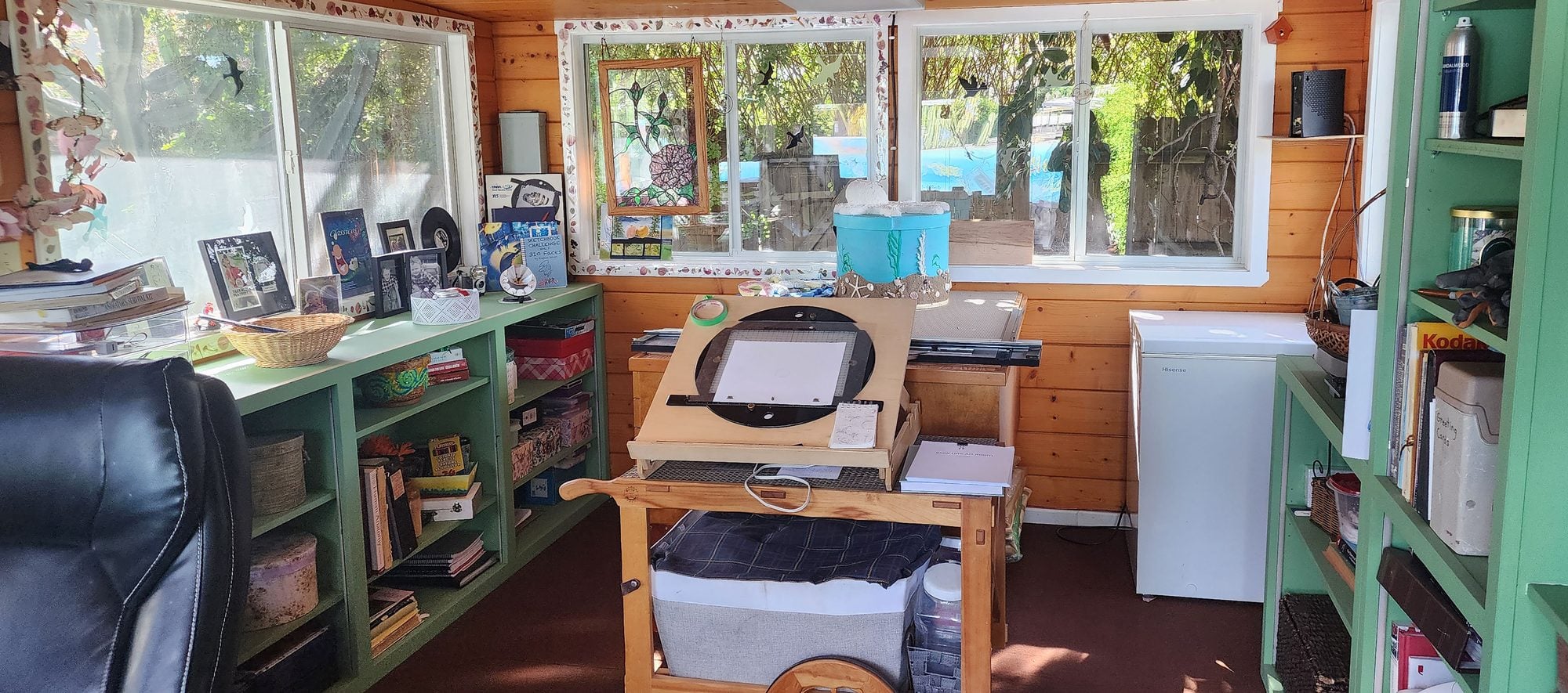 Inside the SlowLine Art Room studio: green bookshelves, a drawing desk and windows looking out to the garden